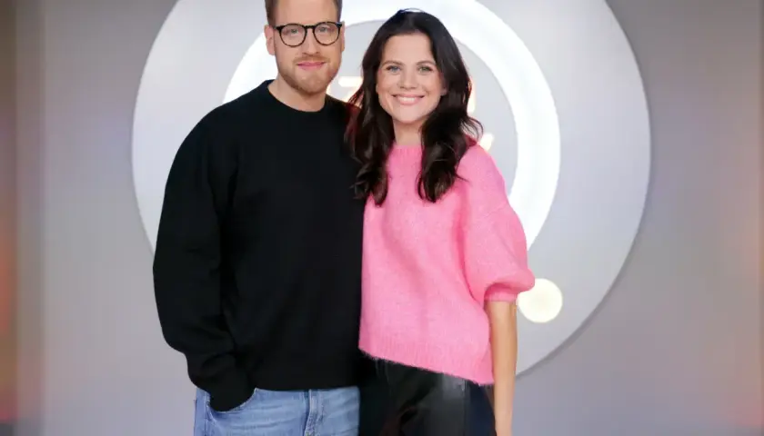 Patrycja Stockinger, dziennikarka, uśmiecha się obok kolegi w studiu telewizyjnym.