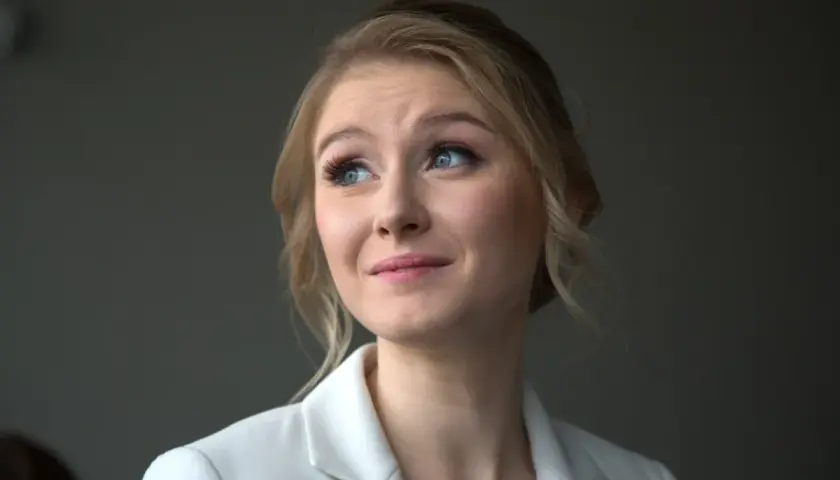 Portret młodej kobiety z blond włosami i niebieskimi oczami, w białej marynarce. Jej wiek to około 30 lat.