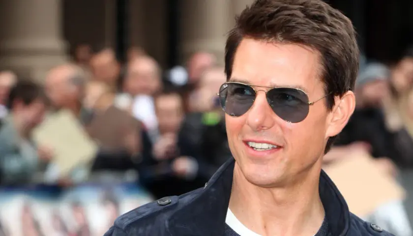 Tom Cruise w okularach przeciwsłonecznych, uśmiecha się. W tle tłum ludzi. Ciekawe, ile lat ma Tom Cruise?