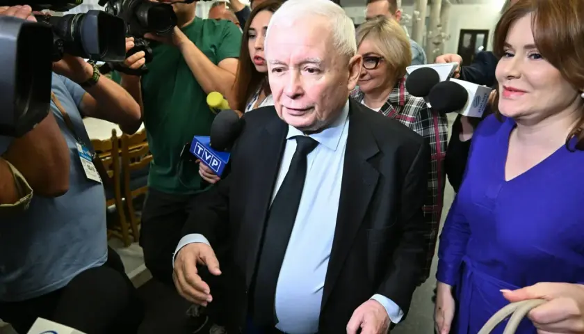 Jarosław Kaczyński otoczony przez dziennikarzy. Wzrost i waga polityka są tematem dyskusji, gdy otaczają go kamery i mikrofony.