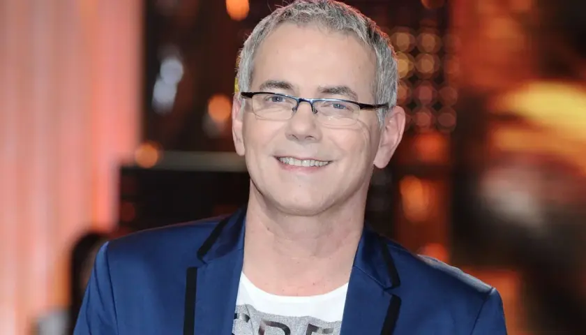 Robert Janowski ile ma lat? Uśmiechnięty mężczyzna w okularach, w granatowej marynarce i białej koszulce.