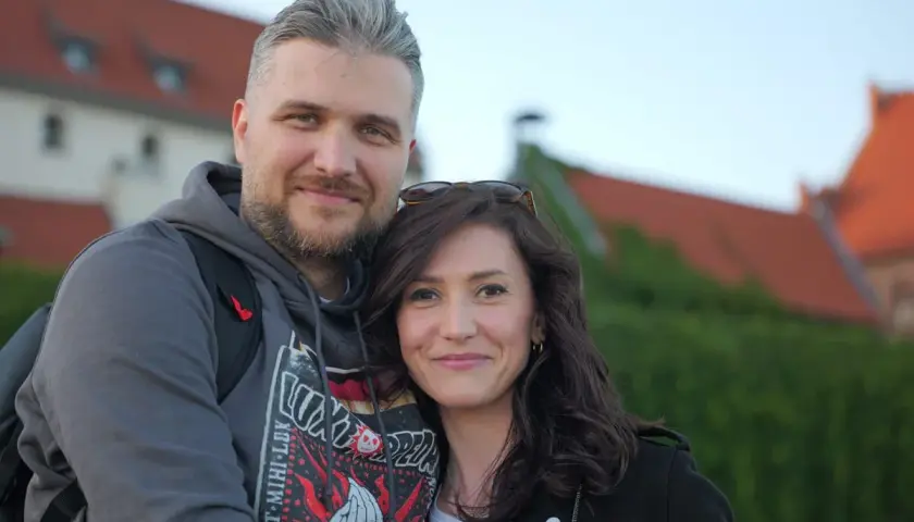 Ewa Zajączkowska-Hernik i jej mąż, uśmiechnięci na tle zabytkowych budynków.