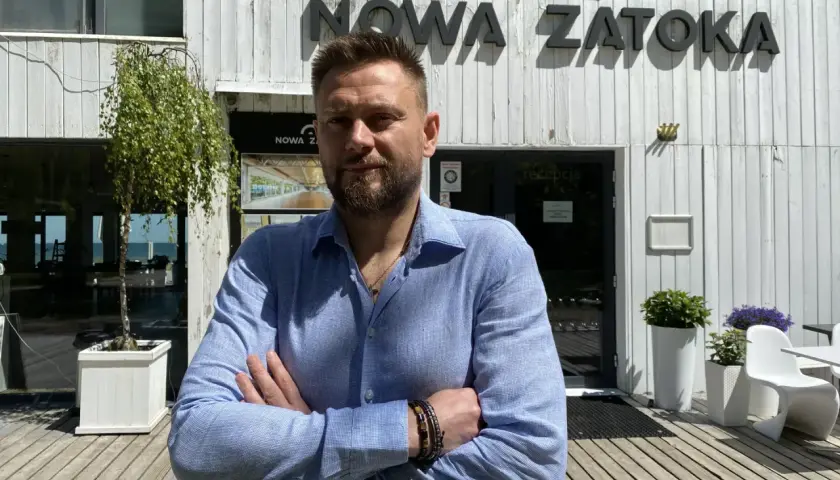 Mężczyzna stoi przed budynkiem z napisem "NOWA ZATOKA".