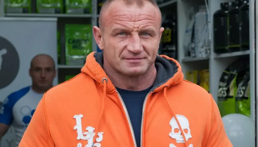 Mariusz Pudzianowski, znany jako Pudzian, w pomarańczowej bluzie z kapturem. Ile lat ma Pudzian? To pytanie nurtuje wielu fanów.