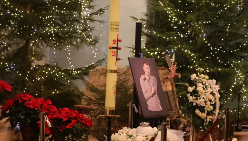 Uroczystość pogrzebowa Krzysztofa Respondka. W tle choinki ozdobione lampkami, obok portret zmarłego, świeca paschalna i białe kwiaty.