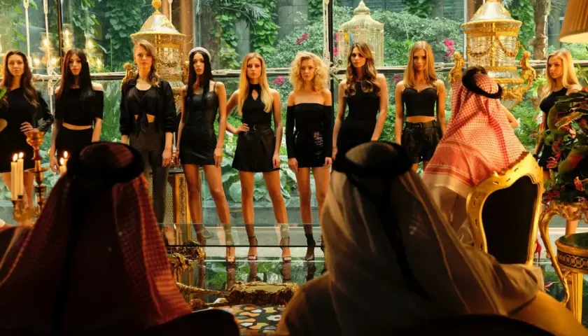 Scena z afery dubajskiej: kobiety w czarnych strojach prezentują się przed mężczyznami w tradycyjnych arabskich strojach.