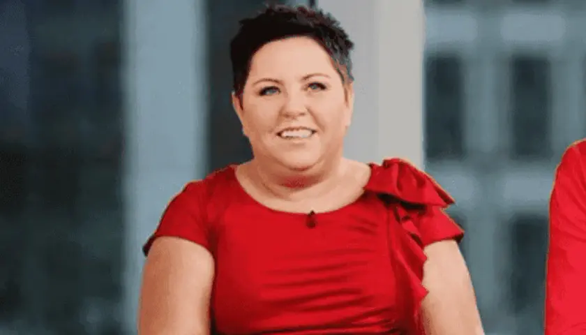 Uśmiechnięta Dorota Wellman w czerwonej sukience. Jej wiek nie jest widoczny, ale emanuje pewnością siebie.