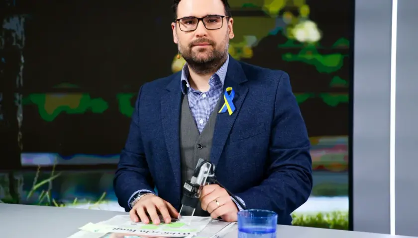Michał Sznajder, w garniturze z niebiesko-żółtą wstążką, przygotowuje się do wywiadu. Jego życiorys to historia dziennikarza.