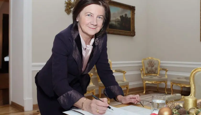 Małgorzata Łaszcz, w eleganckim stroju, pochyla się nad dokumentami. Jej życiorys jest bogaty w doświadczenia.