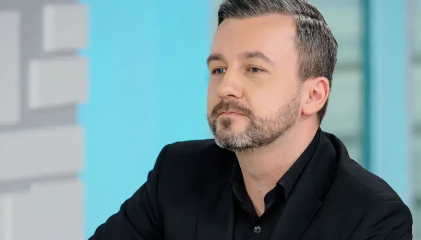 Krzysztof Skórzyński, znany dziennikarz, w czarnym garniturze. Ile ma lat? Trudno zgadnąć, ale wygląda na około 40.