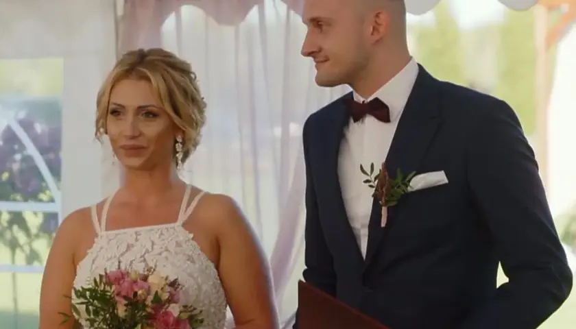 Iza i Kamil, ślub od pierwszego wejrzenia. Panna młoda z bukietem, pan młody w garniturze, patrzą na siebie z uśmiechem.