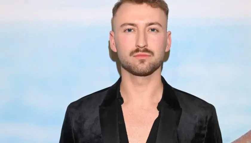 Michał Bartkiewicz w czarnym aksamitnym marynarkowym stroju, z zarostem i fryzurą, na tle błękitnego nieba. Jego życie prywatne budzi zainteresowanie.