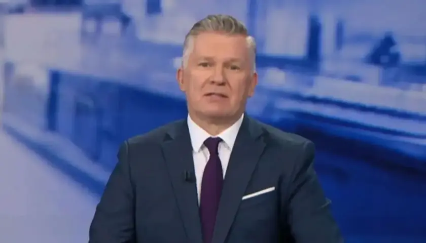 Mężczyzna w garniturze, prowadzący tvn wiadomości, z uwagą przekazuje informacje.
