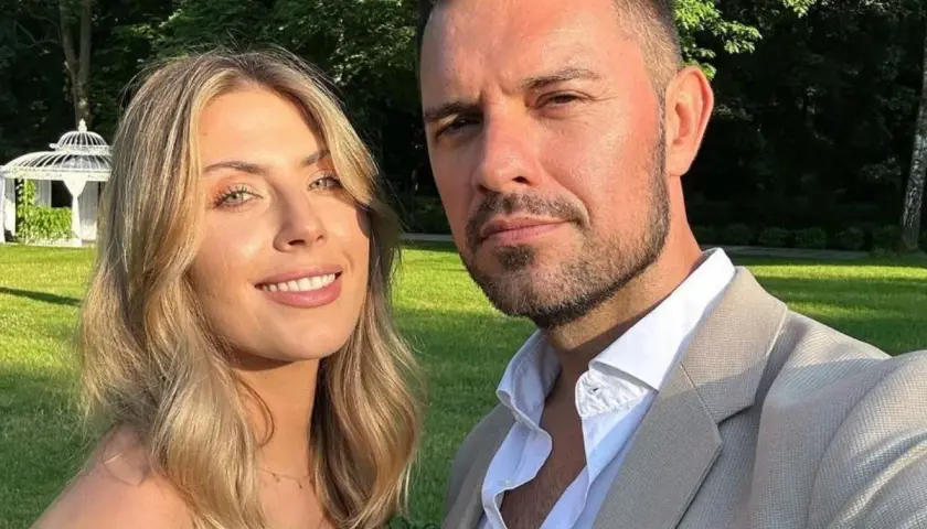 Aleksandra Gryś z mężem na tle ogrodu. Uśmiechnięta para pozuje do zdjęcia w słoneczny dzień.