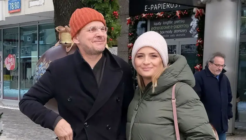 Bartłomiej Topa z żoną w zimowej stylizacji, uśmiechnięci na tle świątecznych dekoracji.