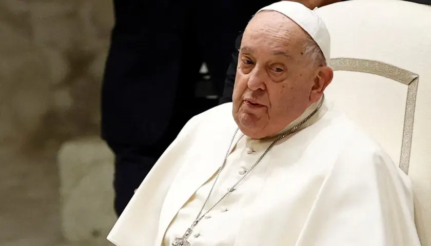 Papież Franciszek, siedzący na białym krześle, w białej sutannie i piusce. Jego wzrost jest typowy dla mężczyzny w jego wieku.