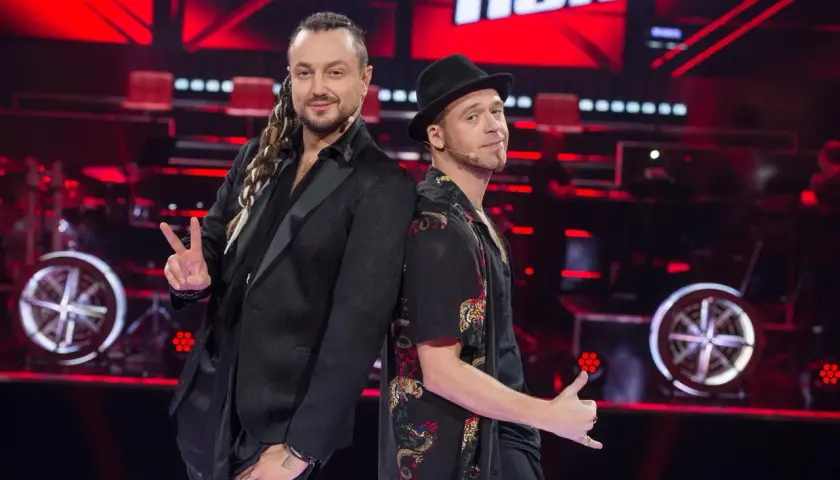 Tomson i Baron, dwaj charyzmatyczni artyści, pozują plecami do siebie na scenie "The Voice of Poland".