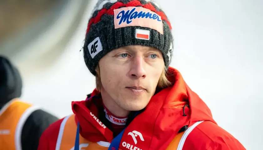 Skoczek narciarski Dawid Kubacki w czapce z napisem "Manner" i flagą Polski. Choć wbrew plotkom Dawid Kubacki nie żyje, jego determinacja na skoczni wciąż inspiruje.
