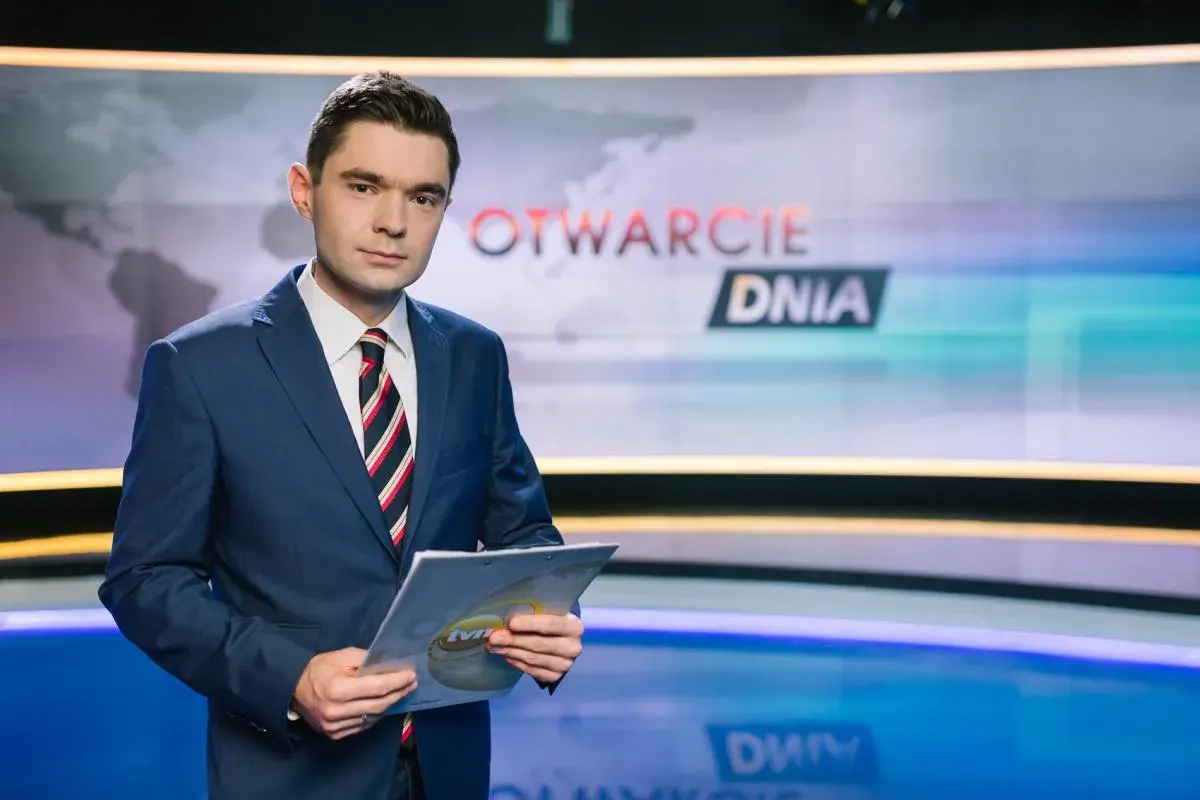 Jan Niedziałek, prezenter "Otwarcie Dnia", w garniturze trzyma dokumenty. Jego życiorys to historia kariery w mediach.