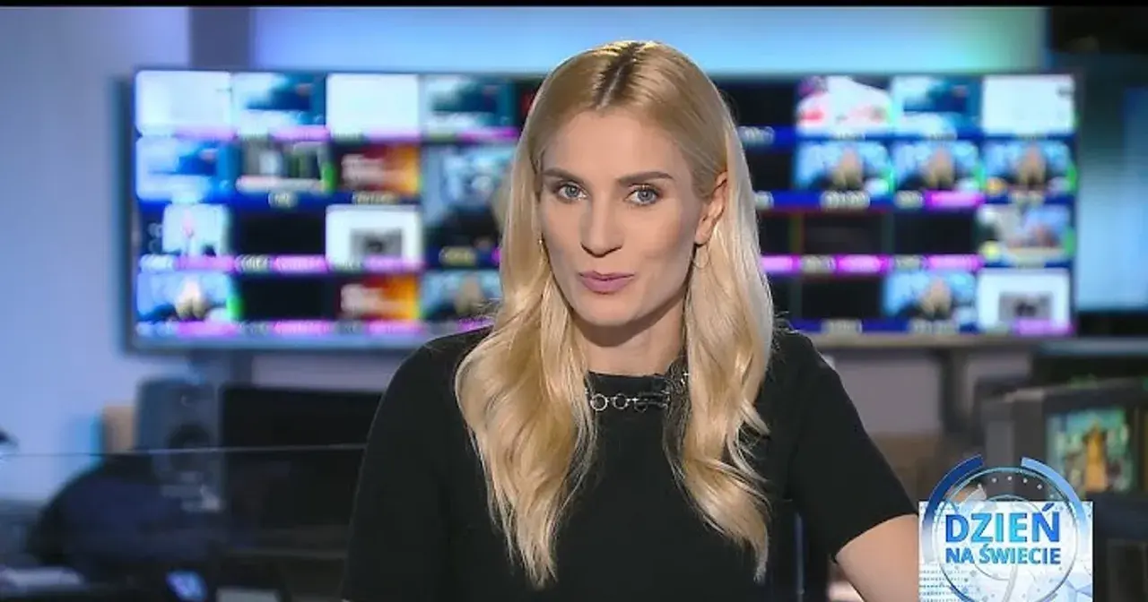 Blond dziennikarka TVN w czarnej bluzce z naszyjnikiem, na tle monitorów.