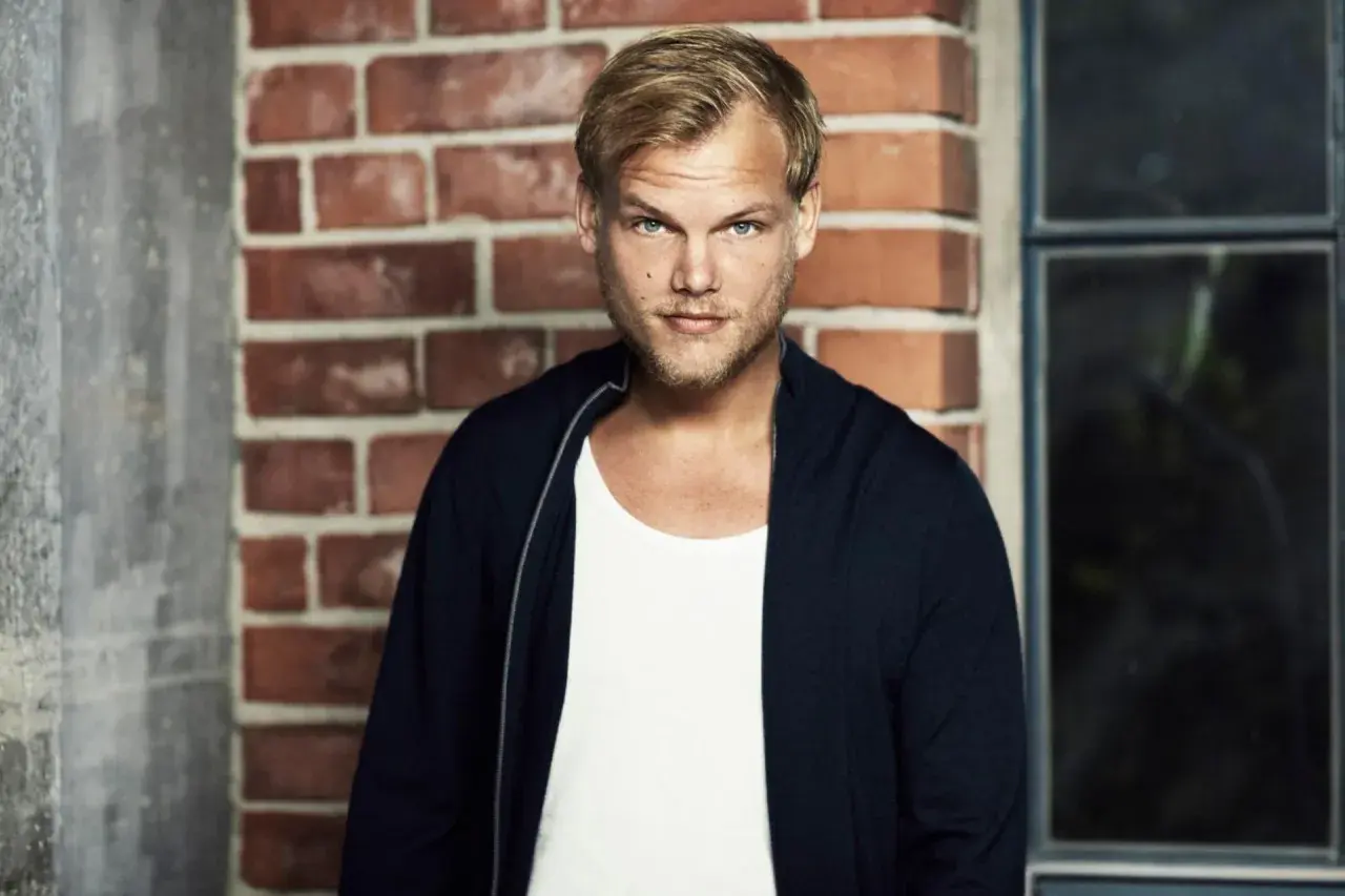 Avicii, w białej koszulce i granatowej bluzie, na tle ceglanej ściany. Jego pożegnalny list wciąż porusza serca fanów.