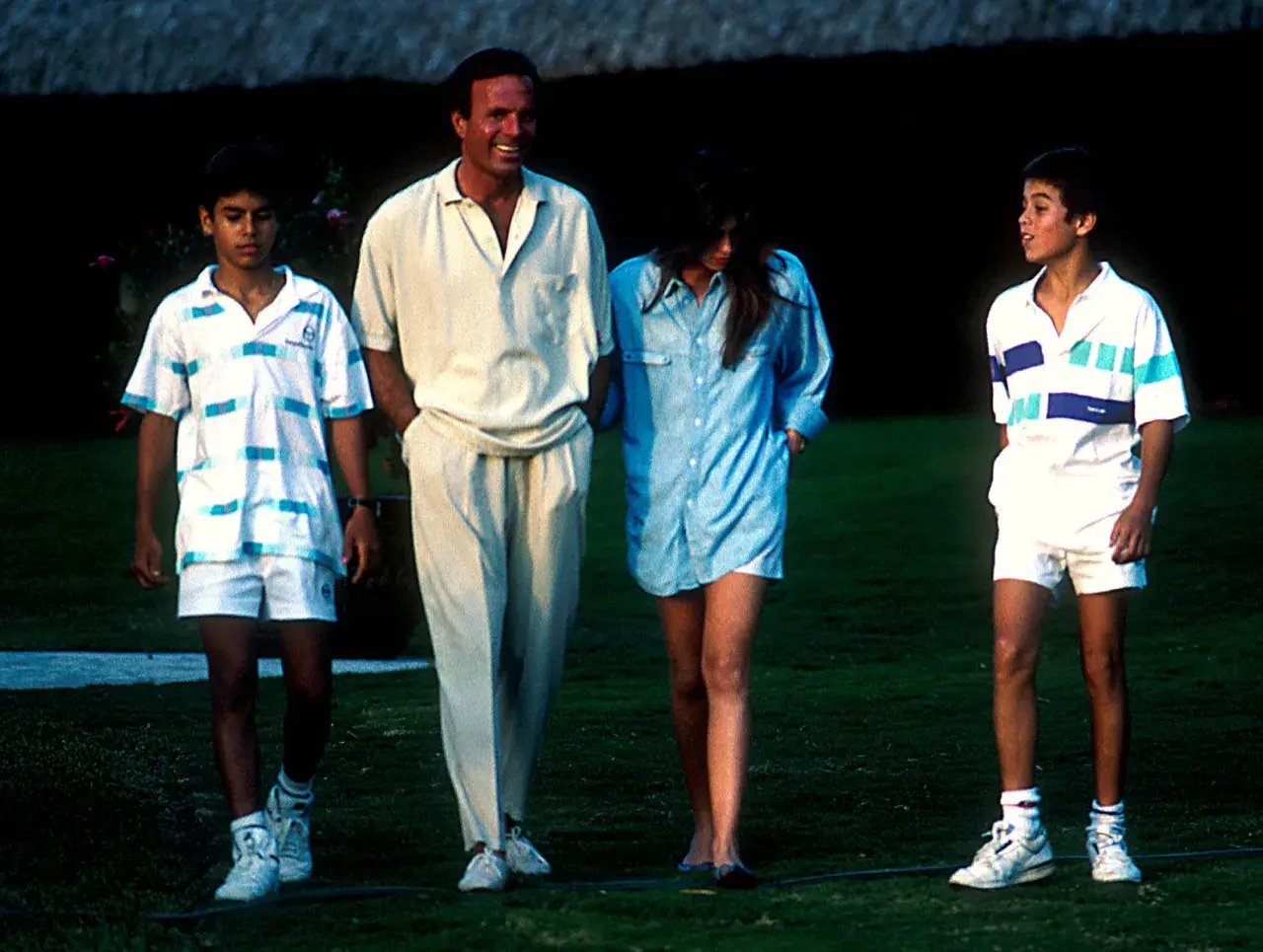 Julio Iglesias z dziećmi, dwoma synami i córką, spacerują po trawniku w letnich strojach.
