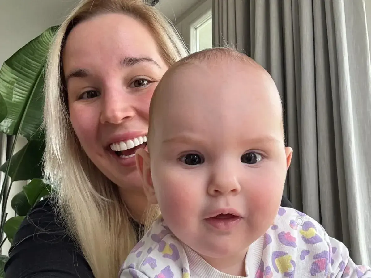 Uśmiechnięta blondynka z dzieckiem na rękach. Dziecko ma ok. 1 roku, a jego wiek to ile lat ma lil masti.
