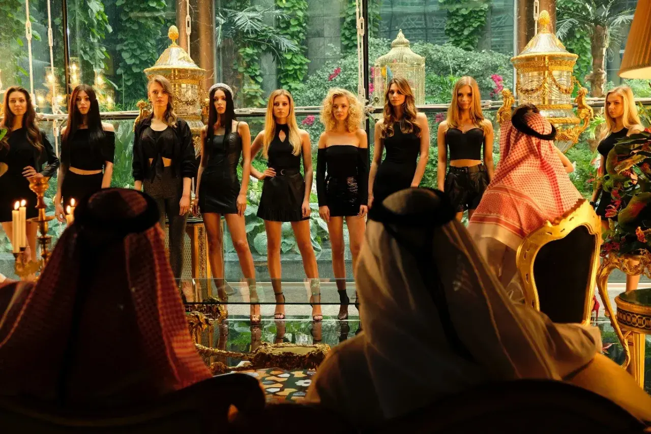 Scena z afery dubajskiej: kobiety w czarnych strojach prezentują się przed mężczyznami w tradycyjnych arabskich strojach.