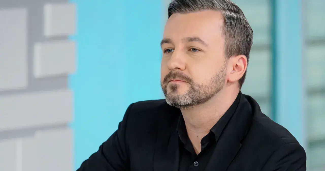 Krzysztof Skórzyński, znany dziennikarz, w czarnym garniturze. Ile ma lat? Trudno zgadnąć, ale wygląda na około 40.