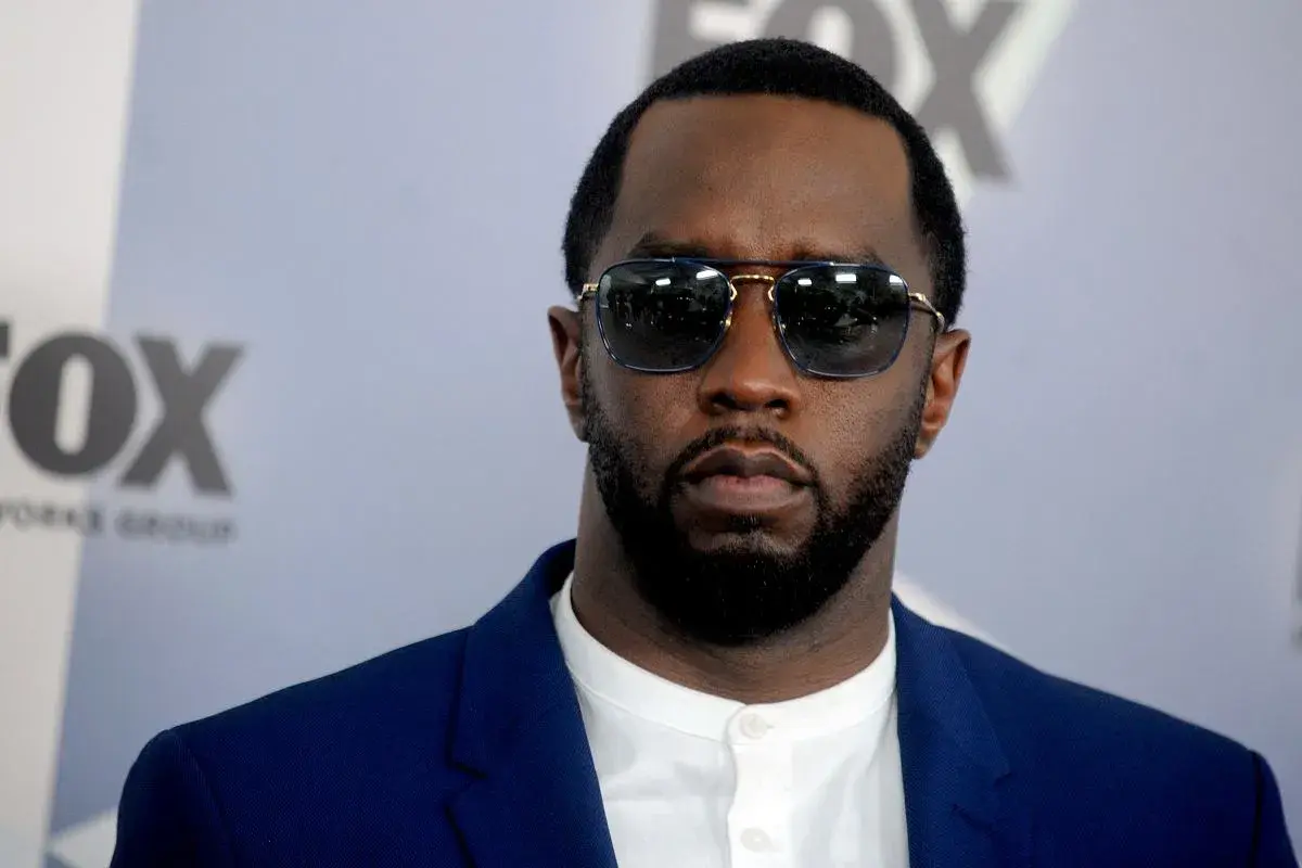 P Diddy w okularach przeciwsłonecznych i niebieskiej marynarce, z logo FOX w tle.