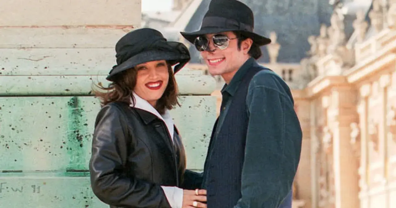 Lisa Marie Presley i jej mąż Michael Jackson w kapeluszach i okularach przeciwsłonecznych, uśmiechnięci na tle budowli.