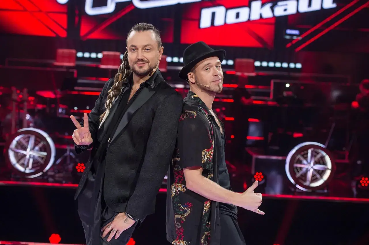 Tomson i Baron, dwaj charyzmatyczni artyści, pozują plecami do siebie na scenie "The Voice of Poland".