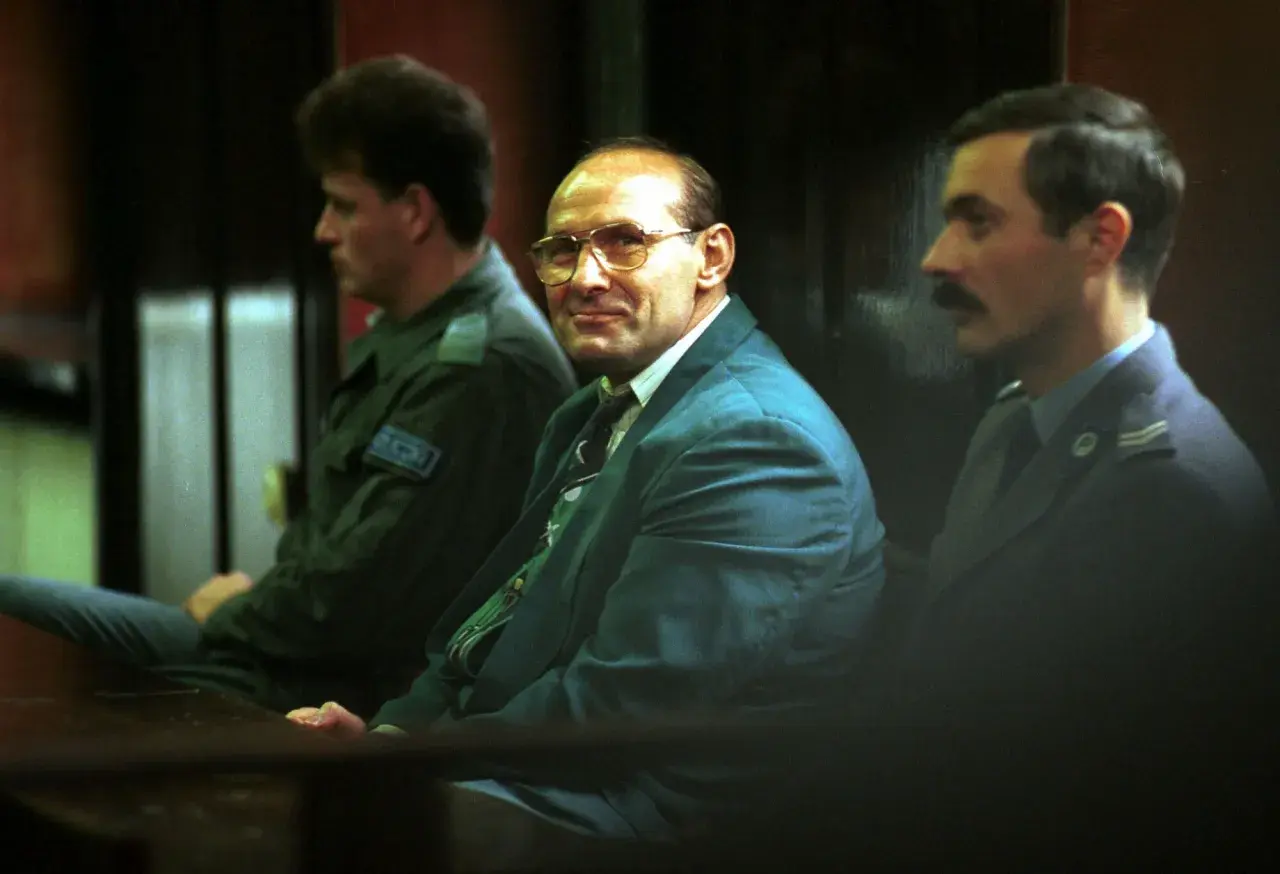 Trzech mężczyzn w garniturach siedzi w sali sądowej. Jeden z nich, w okularach, wygląda jak pershing gangster.