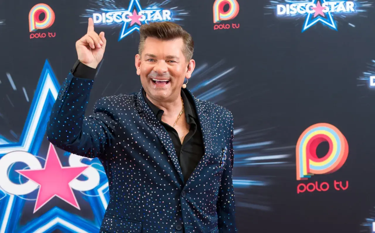 Uśmiechnięty Zenek Martyniuk w błyszczącej marynarce, pozuje na tle logo Polo TV. Ciekawe, ile lat ma Zenek Martyniuk?