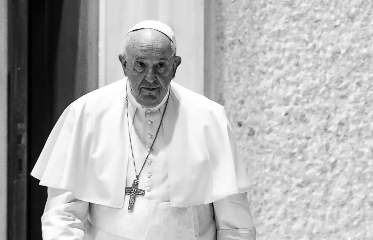 Papież Franciszek, mimo swojego wieku, z uwagą spogląda przed siebie. W białej sutannie i z krzyżem na szyi.