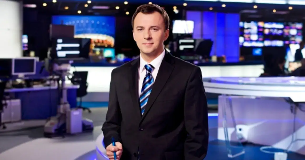 Mężczyzna w garniturze, który mógłby być jednym z byłych dziennikarzy TVN, stoi w studiu telewizyjnym.