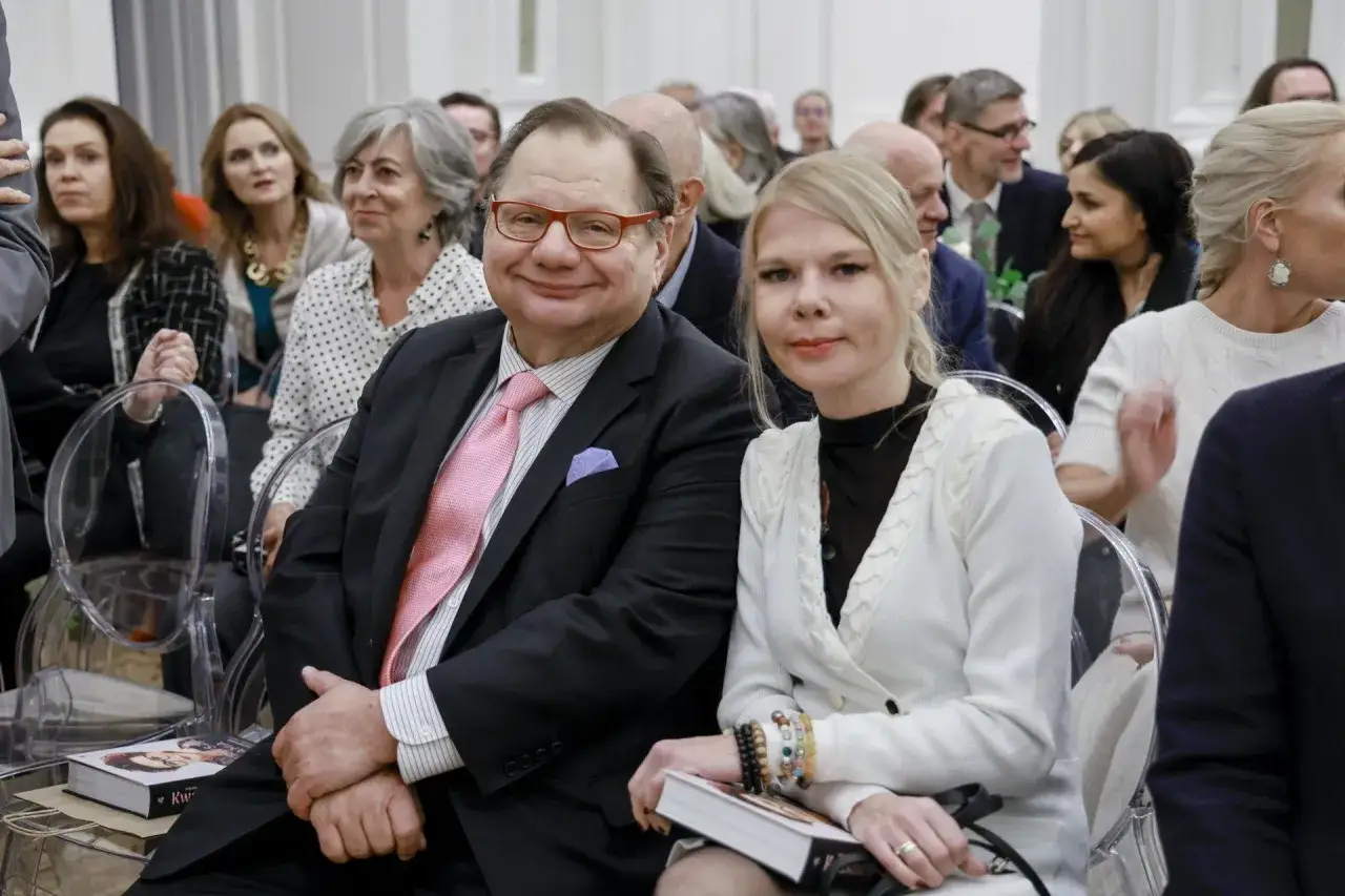 Dominika Lis, wiek nieznany, siedzi obok mężczyzny w garniturze. Oboje patrzą w stronę obiektywu.