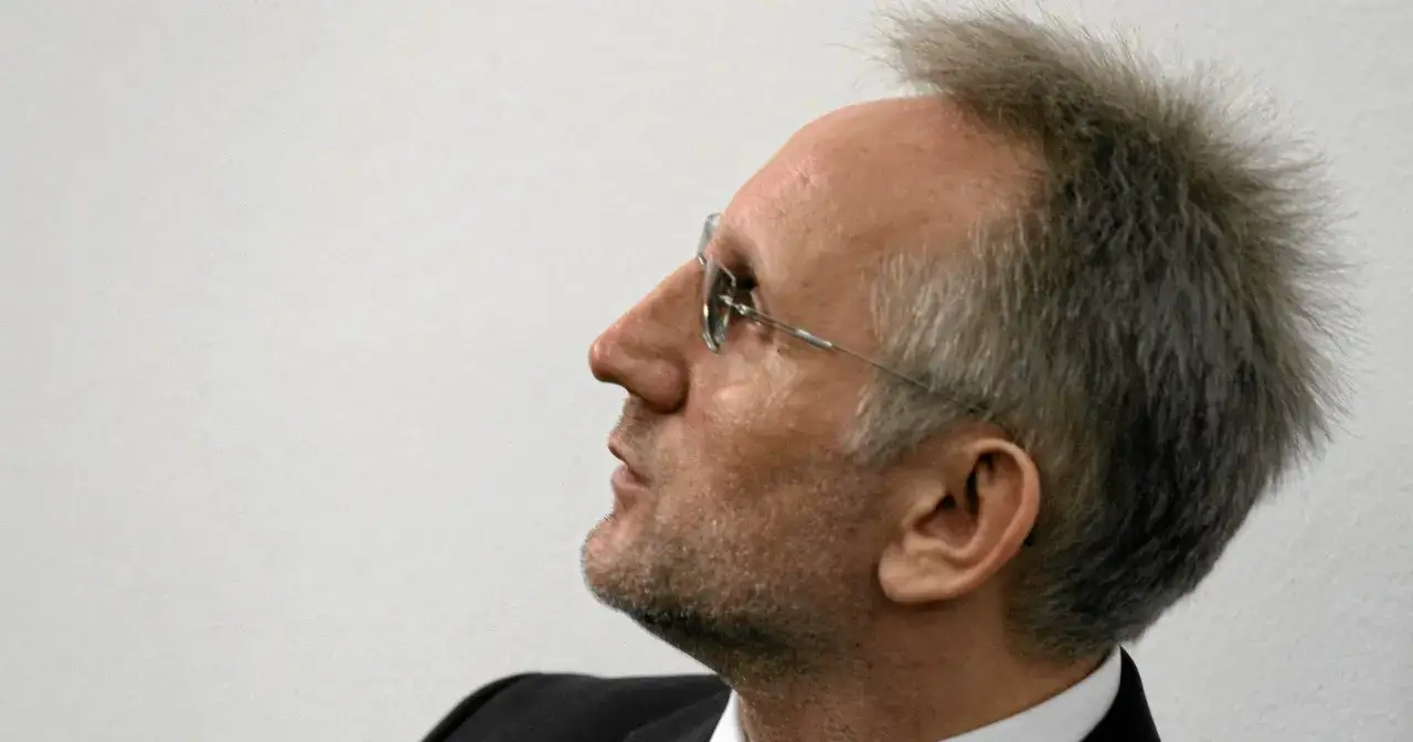 Mężczyzna w okularach, z siwiejącymi włosami, wygląda jakby planował coś niecnego, niczym słowik gangster.