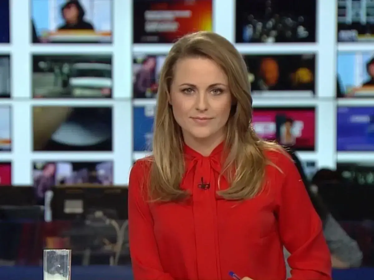 Marta Kłos w czerwonej bluzce, na tle ekranów informacyjnych. Jej biografia to historia sukcesu w mediach.