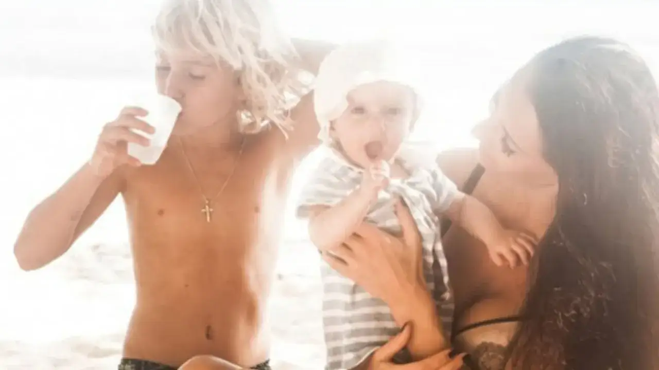 Justyna Steczkowska z dwójką dzieci na plaży. Starszy syn pije wodę, a młodsze dziecko trzyma mama.