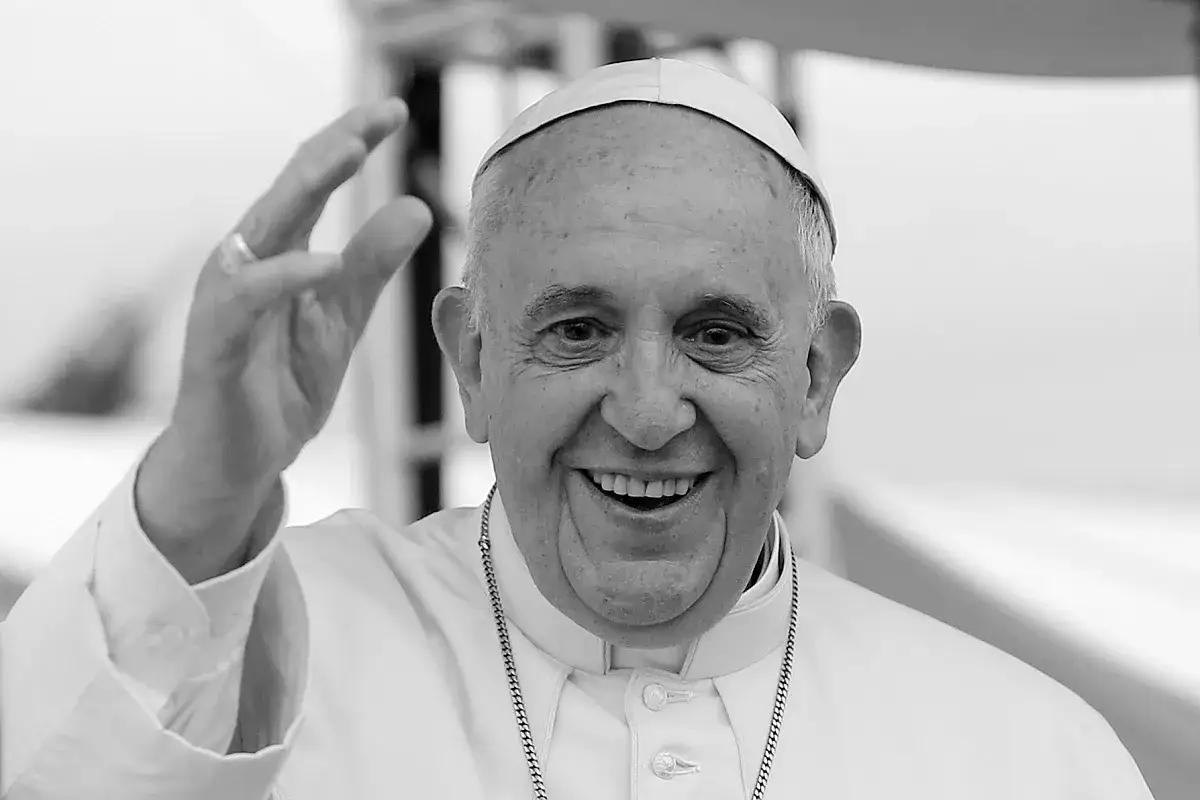 Uśmiechnięty papież Franciszek, którego wiek widać po zmarszczkach, pozdrawia.