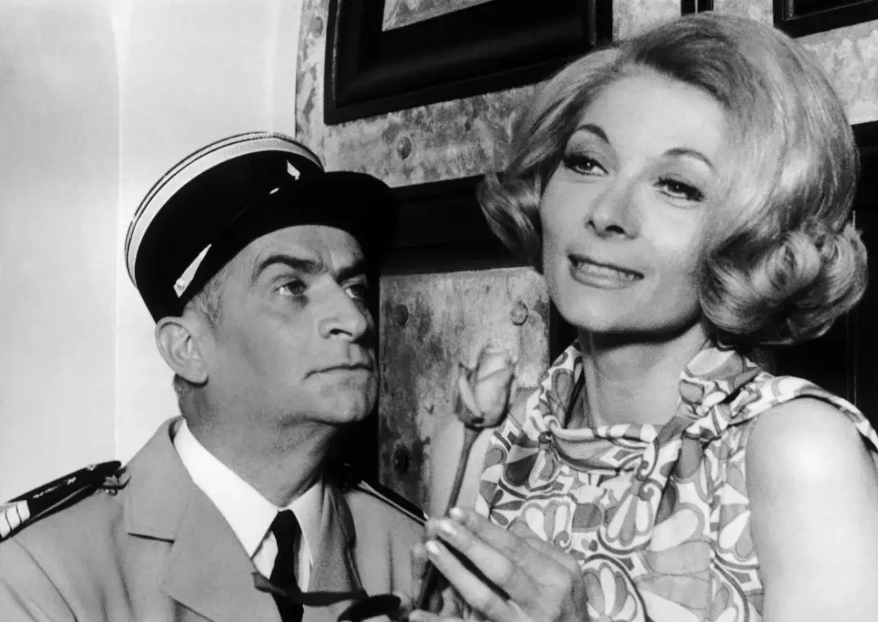Louis de Funès w mundurze patrzy na swoją żonę, która trzyma różę.