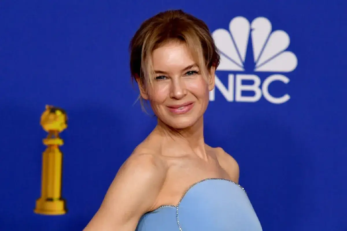 Renee Zellweger, uśmiechnięta, w błękitnej sukni, z Złotym Globem i logo NBC w tle. Choć nie ma tu dzieci, jej uśmiech sugeruje szczęście.