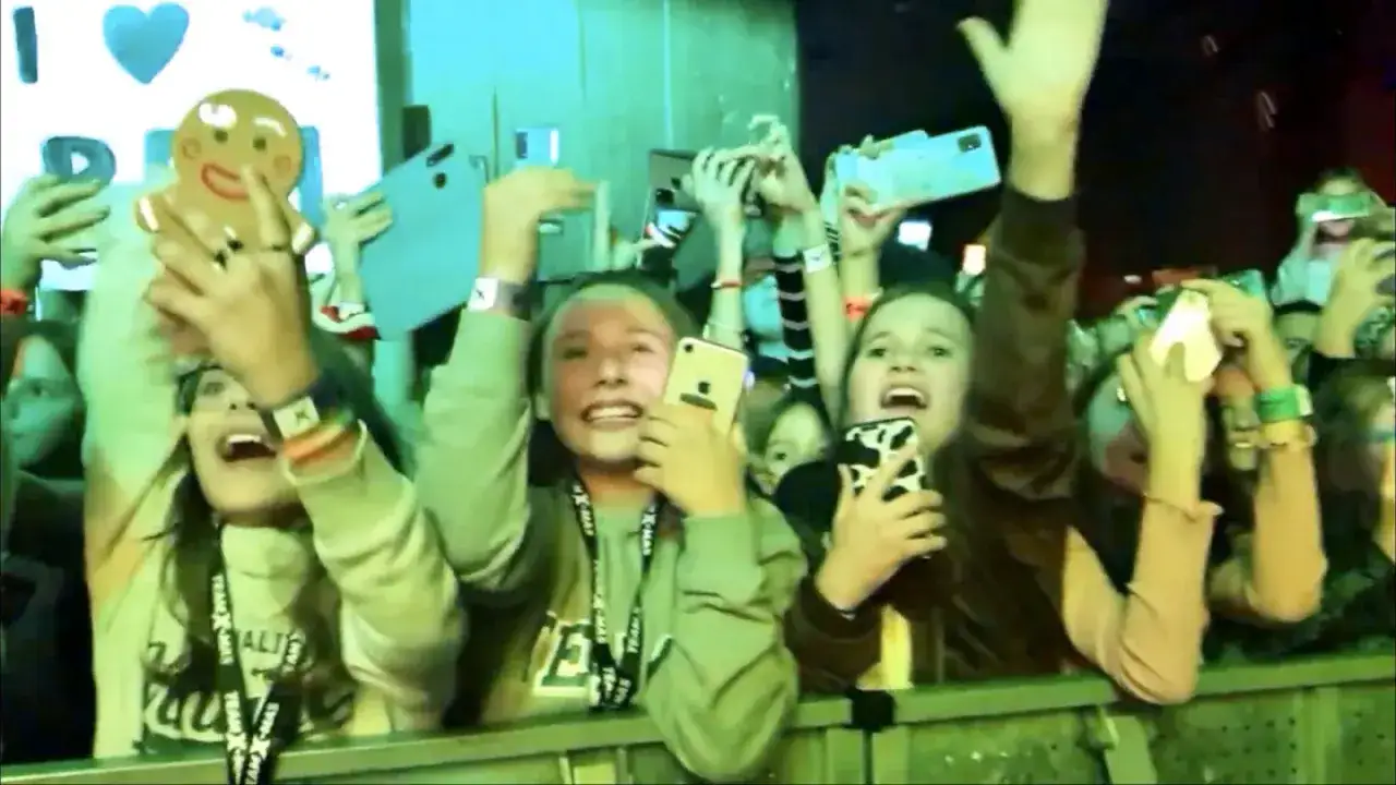 Fani na koncercie Team X camp, z telefonami i ludzikiem z piernika, krzyczą z radości.