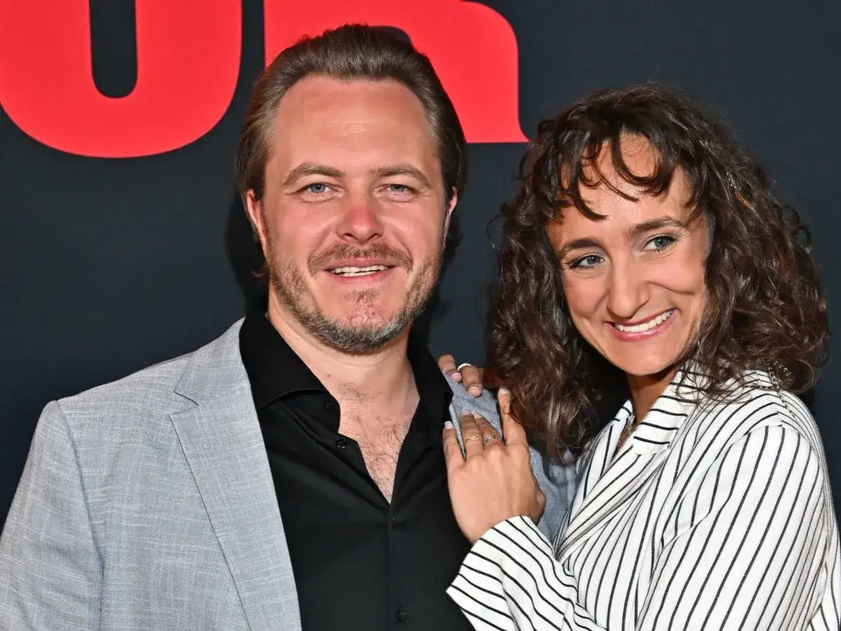 Uśmiechnięci Kamila Kuboth Schuchardt i jej partner pozują do zdjęcia na tle czerwonego napisu.