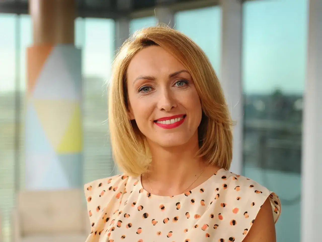 Uśmiechnięta blondynka, jedna z dziennikarki TVN, w bluzce w kropki.