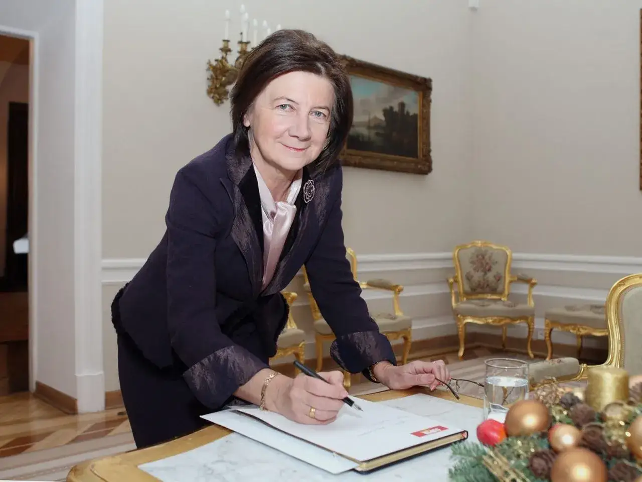Małgorzata Łaszcz, w eleganckim stroju, pochyla się nad dokumentami. Jej życiorys to historia sukcesu.