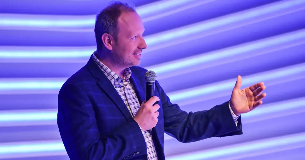 Marcin Majewski z TVN przemawia do publiczności, trzymając mikrofon i gestykulując.