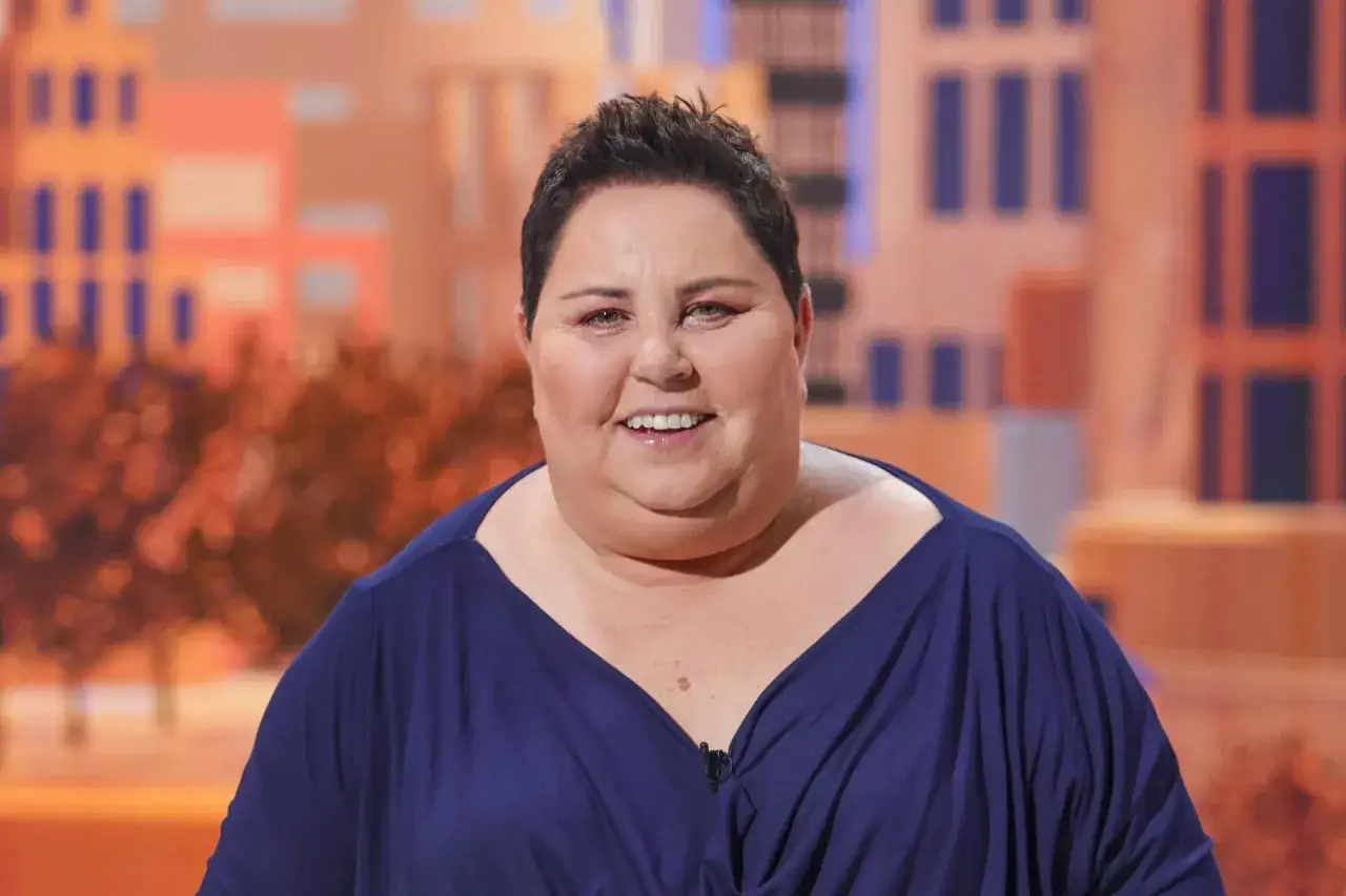 Uśmiechnięta Dorota Wellman, której wiek dodaje jej uroku, w granatowej sukience. Tło sugeruje studio telewizyjne.