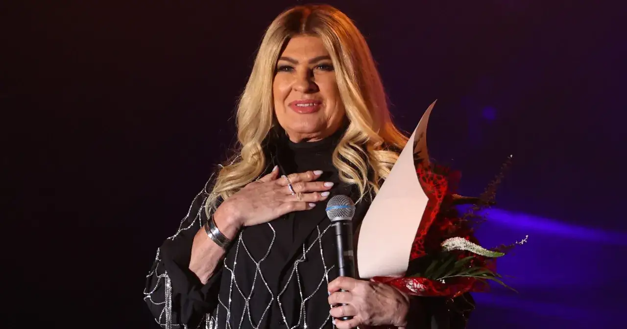 Beata Kozidrak, mimo upływu lat, wciąż zachwyca na scenie. Wokalistka trzyma bukiet kwiatów i mikrofon.